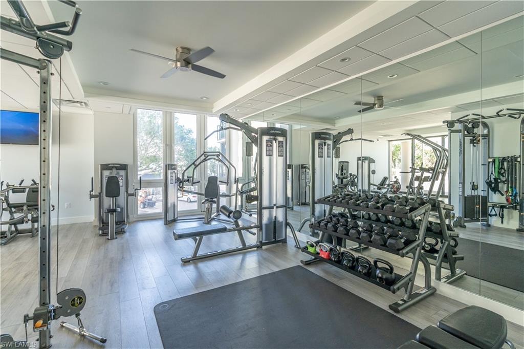 Exercise room with hardwood / wood-style floors, ceiling fan, and a raised ceiling