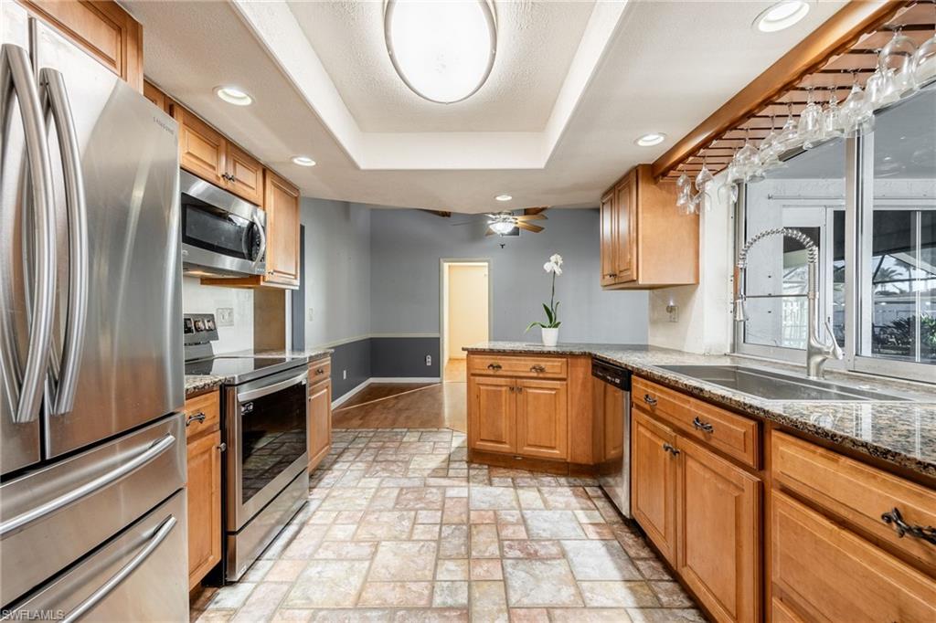 Kitchen with sink, appliances with stainless steel finishes, dark stone countertops, a tray ceiling, and kitchen peninsula