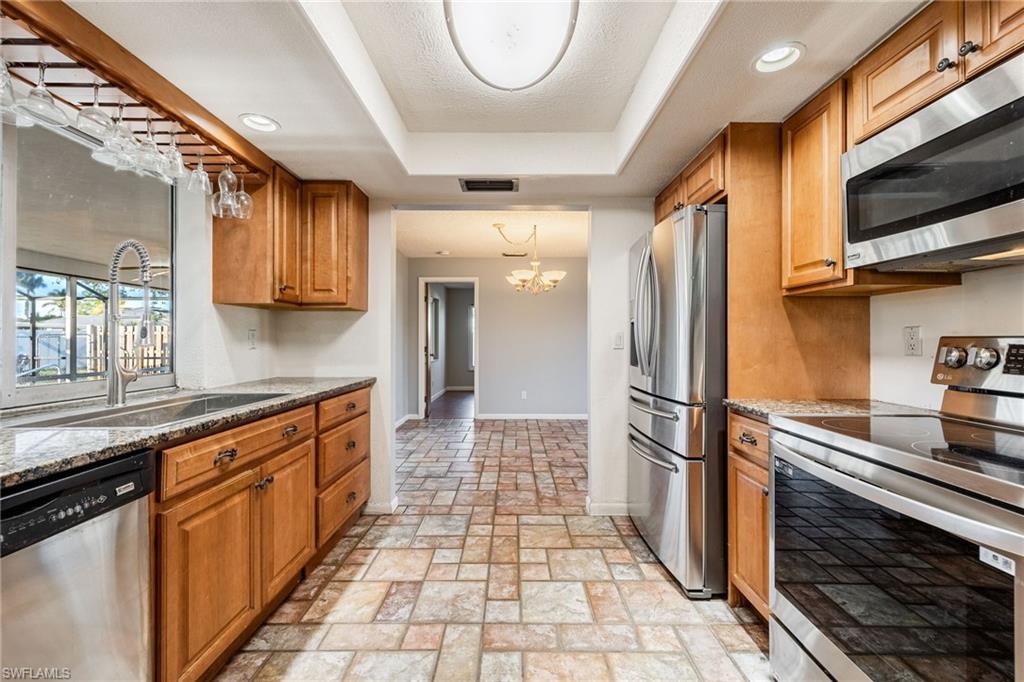 Kitchen with sink, a chandelier, dark stone counters, a raised ceiling, and stainless steel appliances