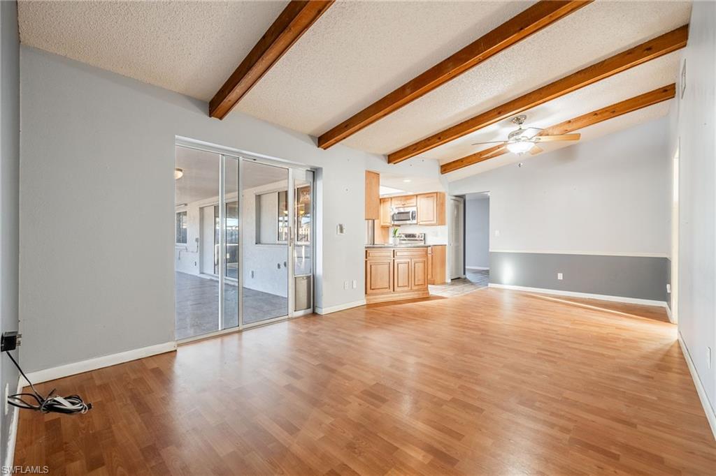 Unfurnished living room featuring ceiling fan, vaulted ceiling with beams, a textured ceiling, and light wood-type flooring