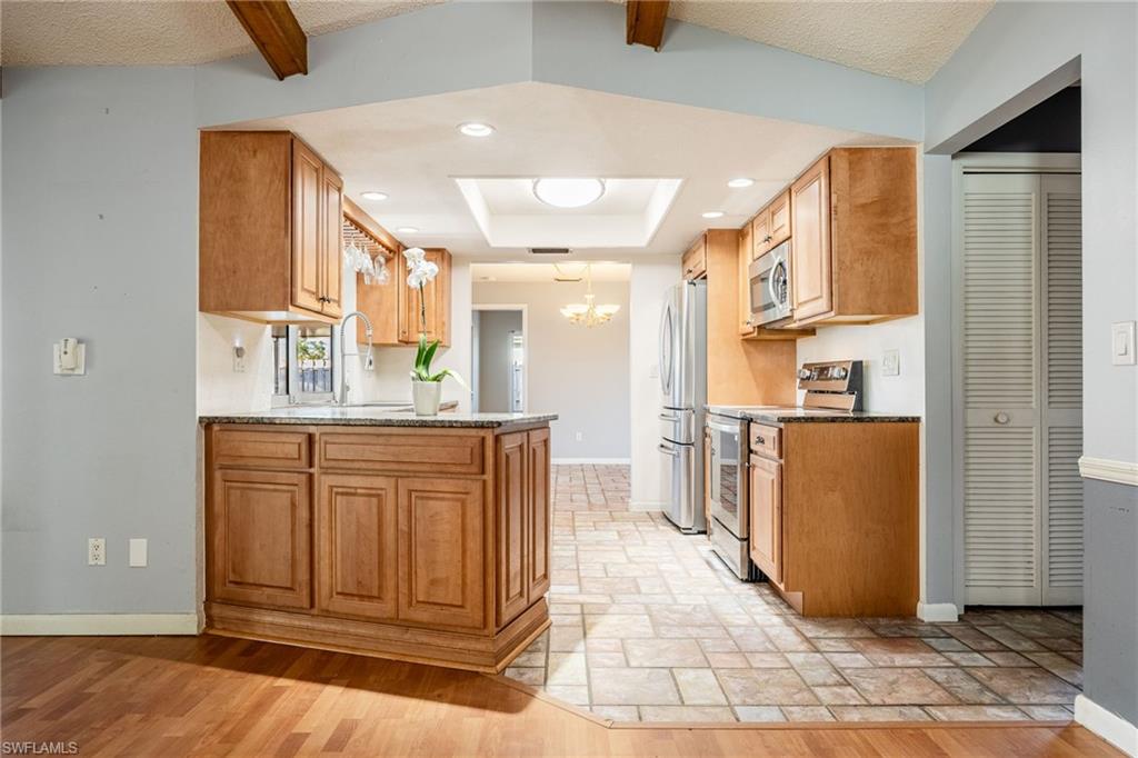 Kitchen with stainless steel appliances, a chandelier, light stone countertops, kitchen peninsula, and beamed ceiling