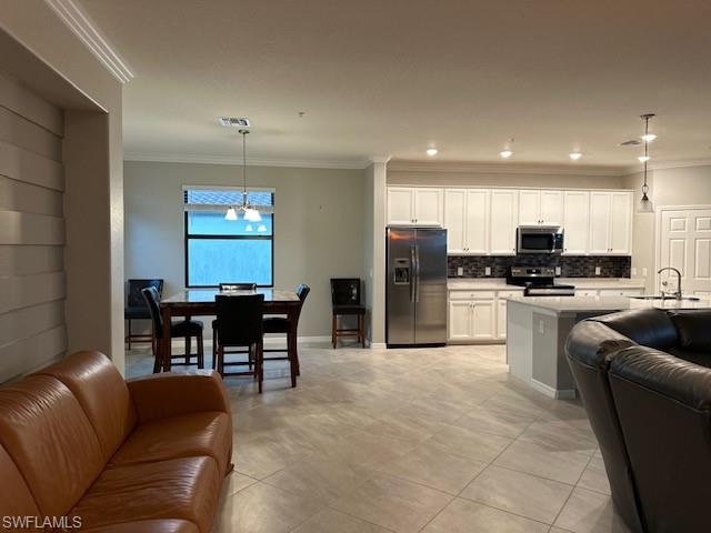 Kitchen featuring stainless steel appliances, light stone counters, ornamental molding, white cabinets, and decorative light fixtures