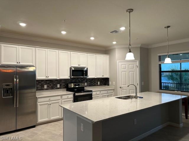 Kitchen with sink, hanging light fixtures, stainless steel appliances, white cabinets, and a center island with sink