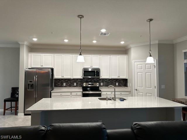 Kitchen with sink, light stone counters, hanging light fixtures, a center island with sink, and stainless steel appliances