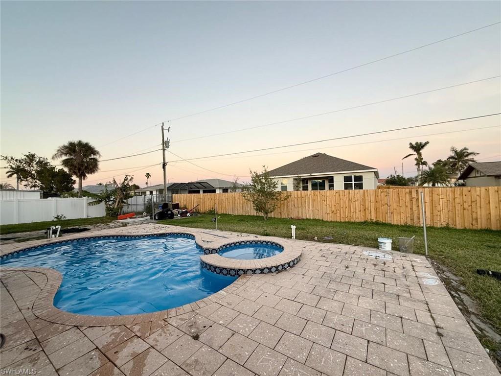 Pool at dusk featuring a yard, an in ground hot tub, and a patio area