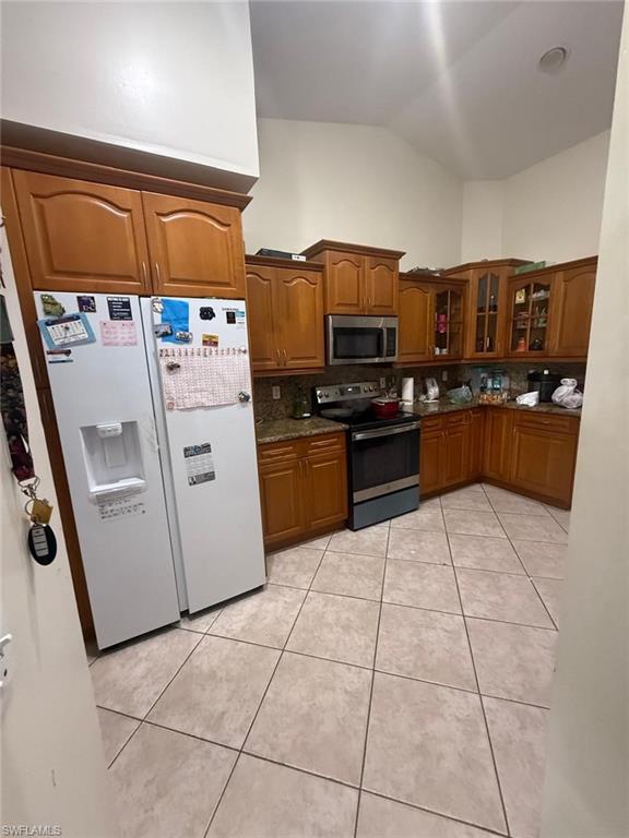 Kitchen with appliances with stainless steel finishes, light tile patterned floors, lofted ceiling, and decorative backsplash