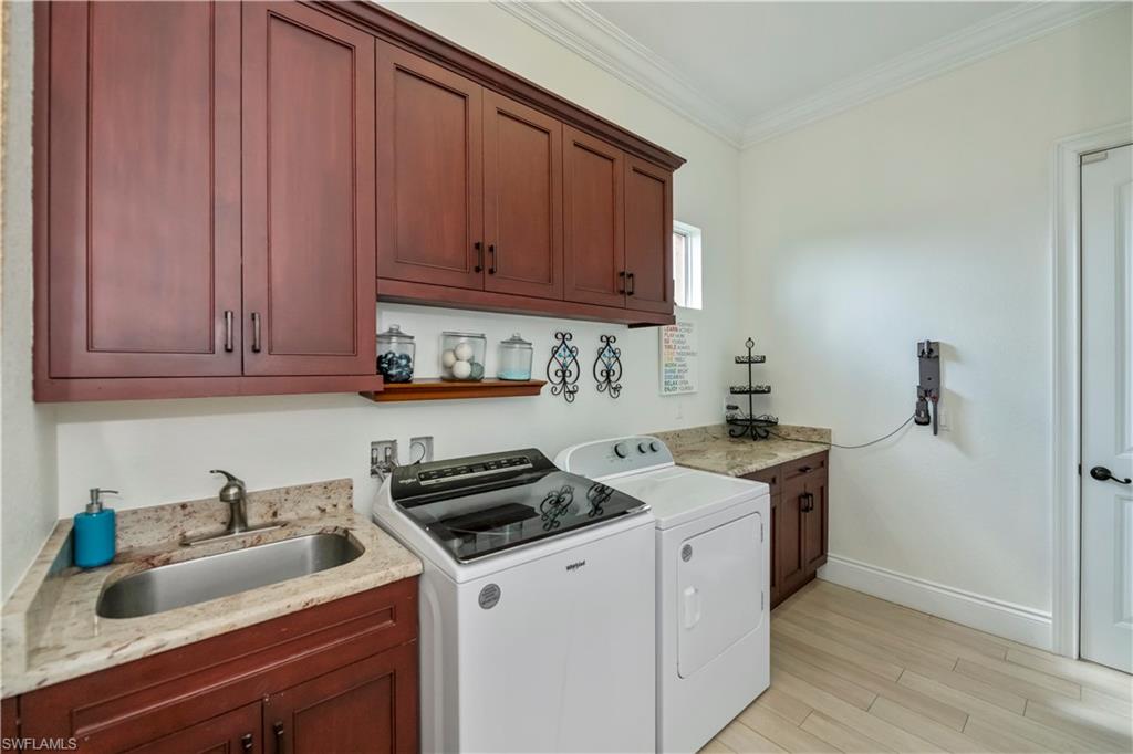 Clothes washing area featuring sink, cabinets, ornamental molding, washing machine and dryer, and light wood-type flooring