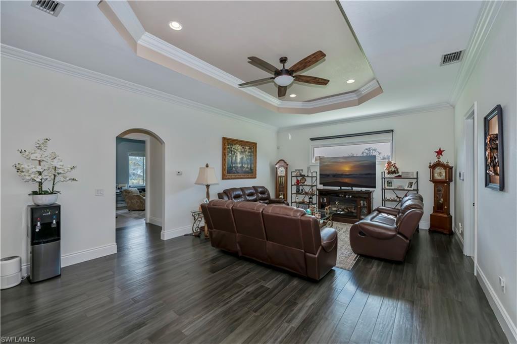 Living room featuring ceiling fan, ornamental molding, dark hardwood / wood-style floors, and a raised ceiling