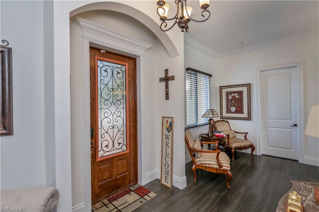Entryway with dark wood-type flooring, ornamental molding, and a notable chandelier