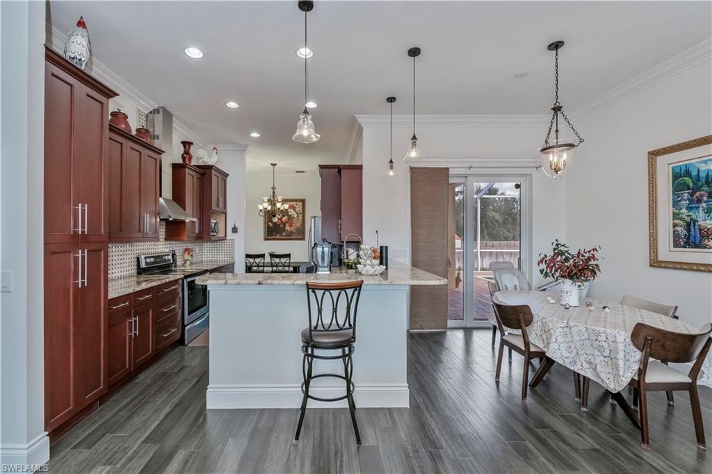 Kitchen featuring stainless steel electric range oven, a breakfast bar, decorative backsplash, hanging light fixtures, and light stone counters