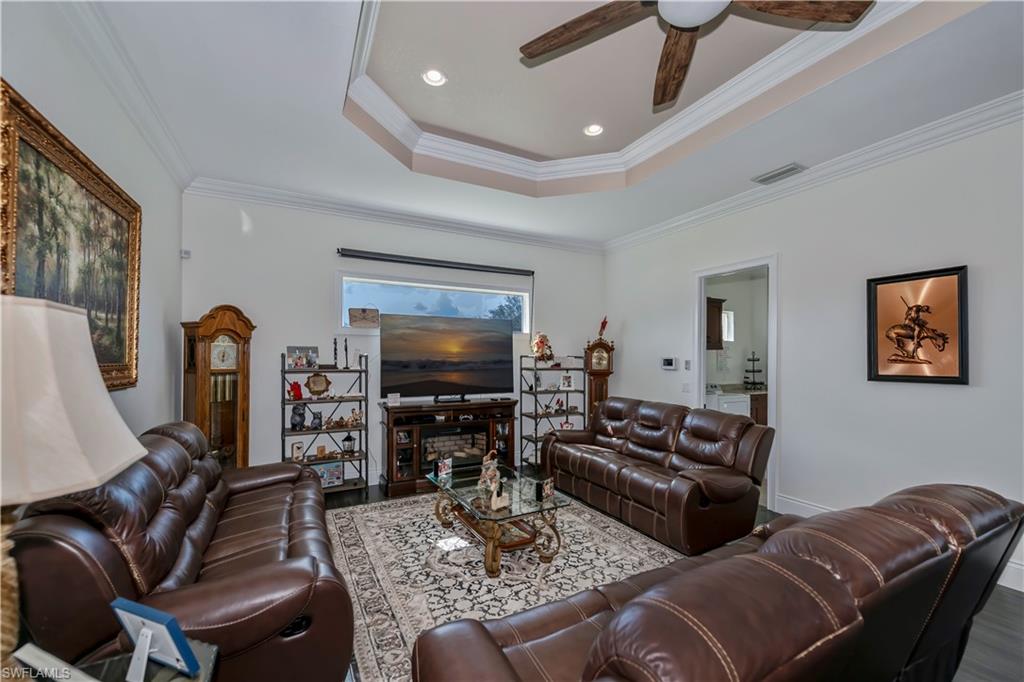Living room featuring hardwood / wood-style floors, a tray ceiling, ornamental molding, and ceiling fan