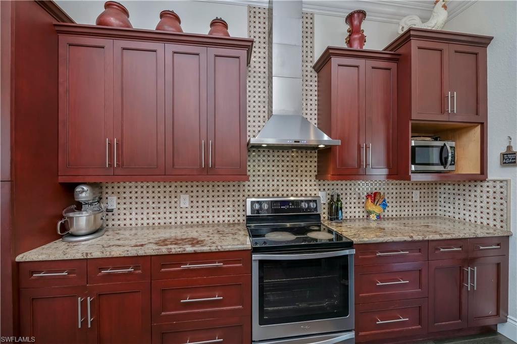 Kitchen with appliances with stainless steel finishes, wall chimney range hood, backsplash, and light stone counters