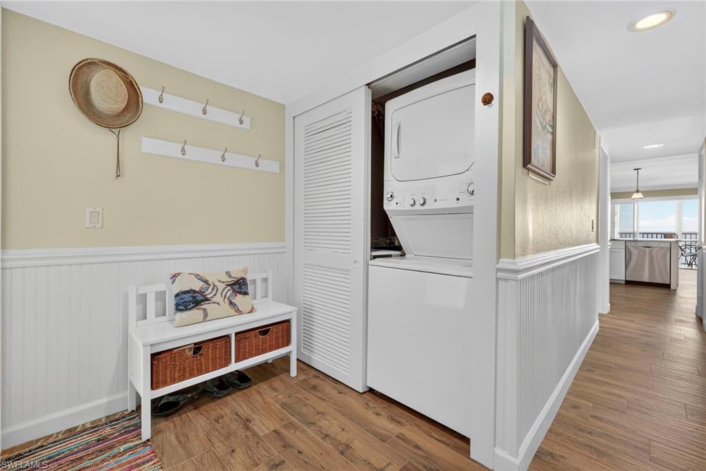 Laundry room featuring wood finished floors, stacked washer / dryer, and wainscoting