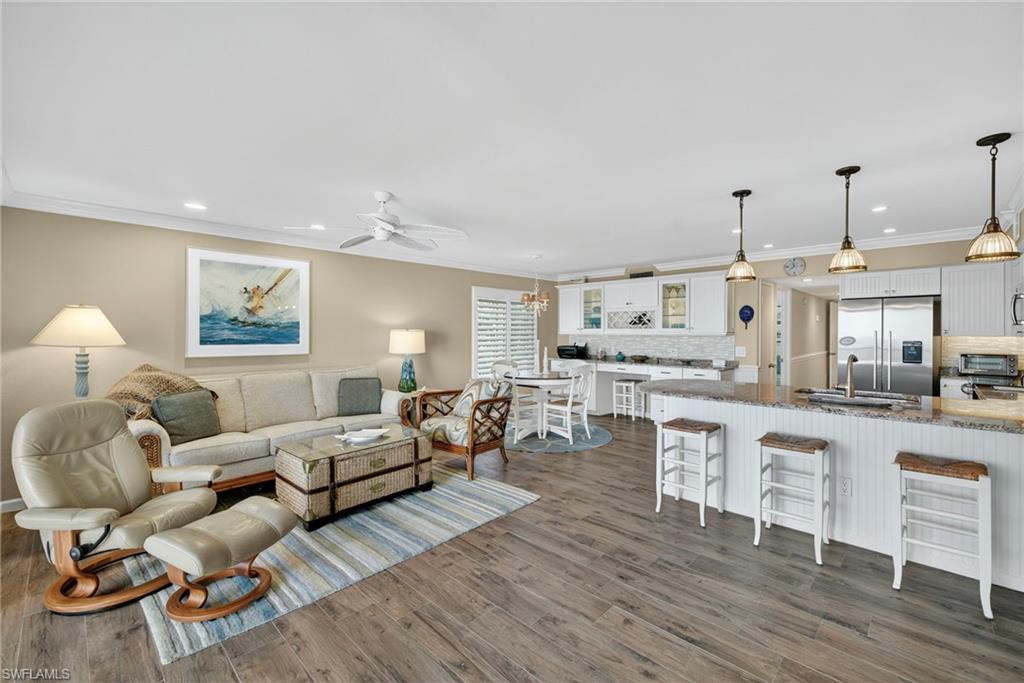 Living room with crown molding, dark wood-style floors, a ceiling fan, recessed lighting, and a chandelier