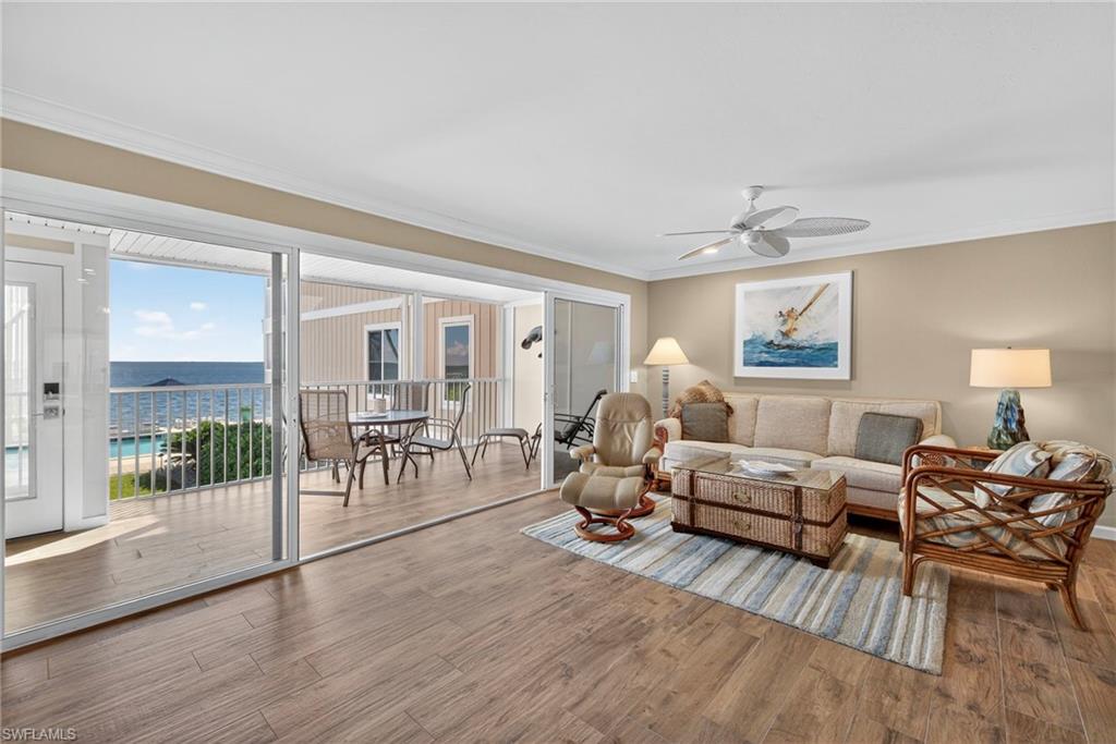 Living area with a water view, ornamental molding, wood finished floors, and a ceiling fan