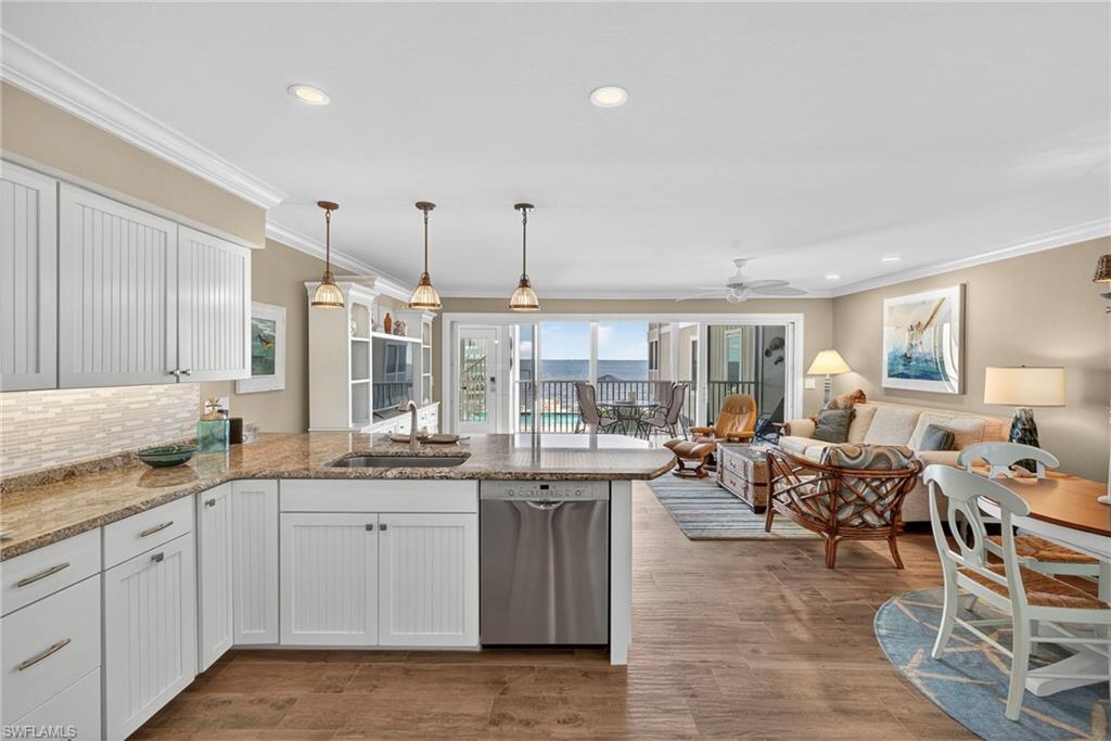 Kitchen featuring white cabinets, ornamental molding, dishwasher, open floor plan, and decorative light fixtures