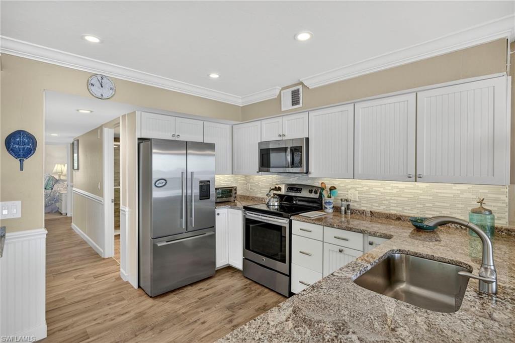 Kitchen featuring stainless steel appliances, light stone countertops, ornamental molding, white cabinetry, and wainscoting