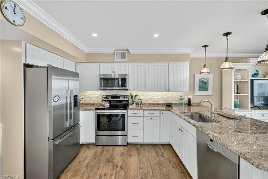 Kitchen featuring appliances with stainless steel finishes, crown molding, white cabinetry, a peninsula, and light stone counters