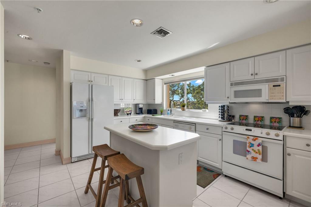 Kitchen with white cabinetry, white appliances, light tile patterned flooring, and a kitchen island