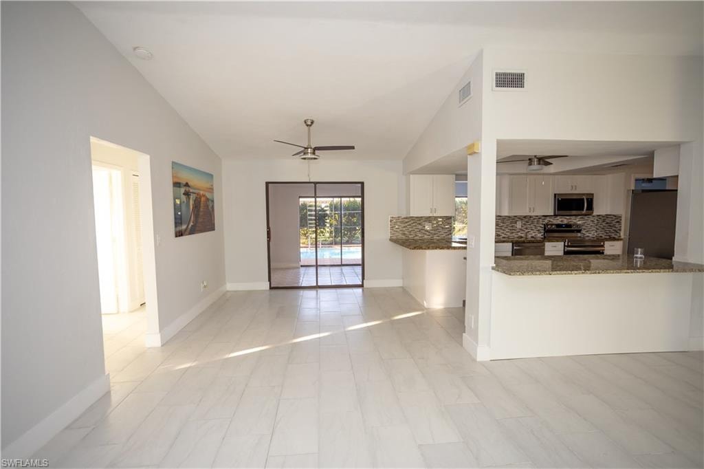 Kitchen featuring ceiling fan, appliances with stainless steel finishes, dark stone countertops, white cabinets, and kitchen peninsula