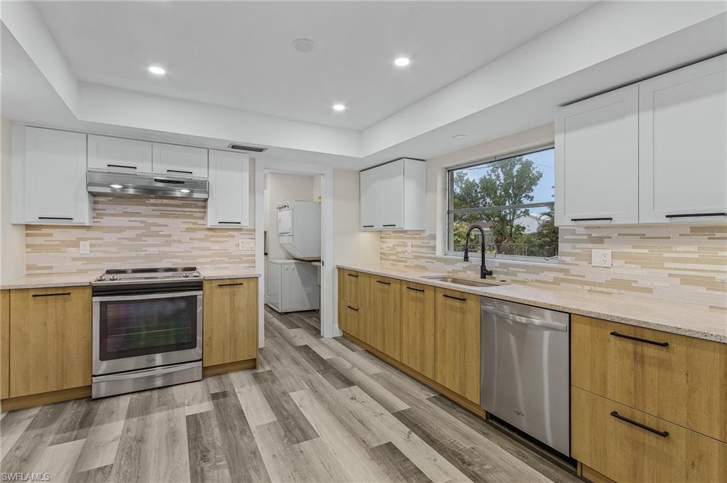 Kitchen featuring stacked washer / drying machine, sink, appliances with stainless steel finishes, light hardwood / wood-style floors, and white cabinets