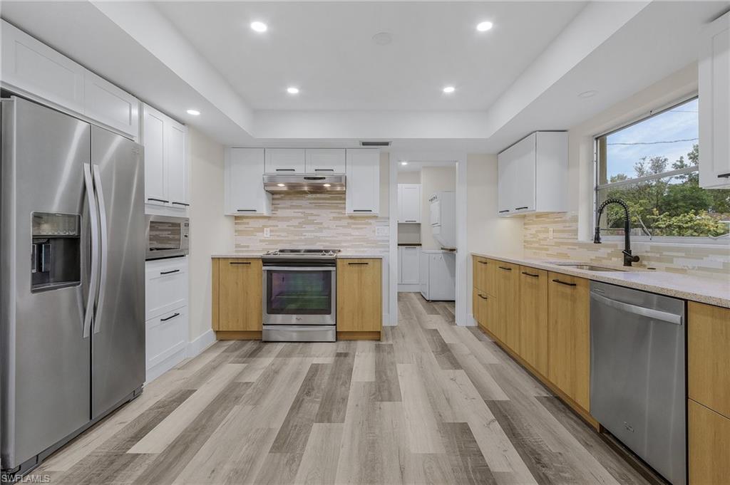 Kitchen with stainless steel appliances, white cabinetry, sink, and a tray ceiling