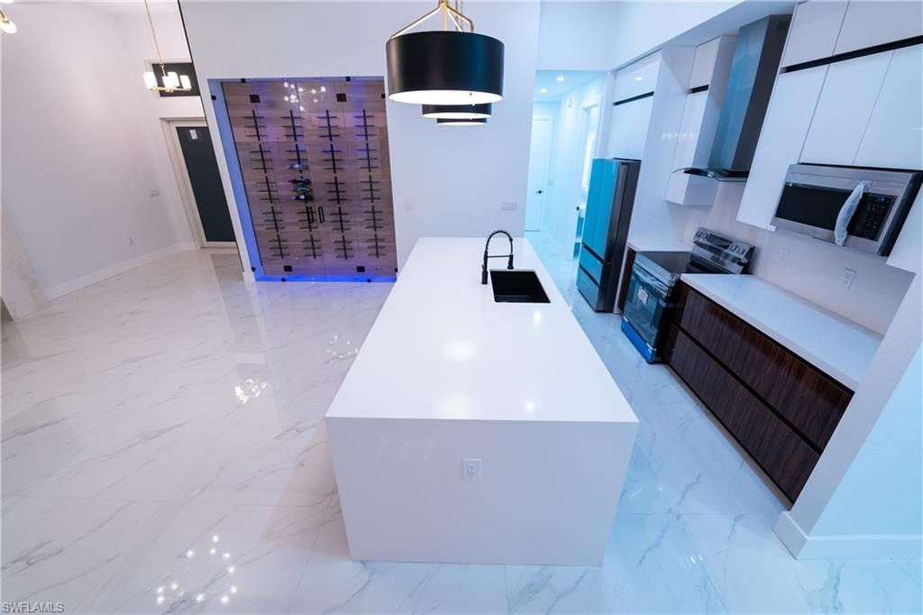 Kitchen with hanging light fixtures, sink, wall chimney range hood, and stainless steel appliances