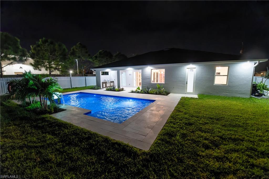 Pool at night featuring a patio, pool water feature, and a yard