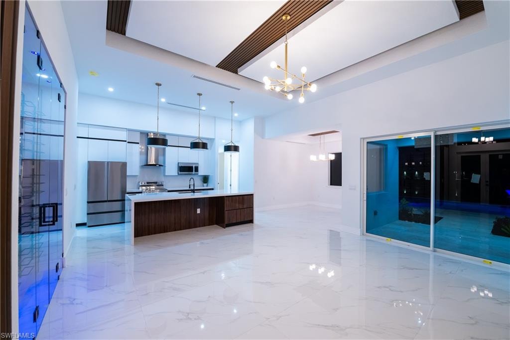 Kitchen with decorative light fixtures, sink, a large island, stainless steel appliances, and wall chimney exhaust hood