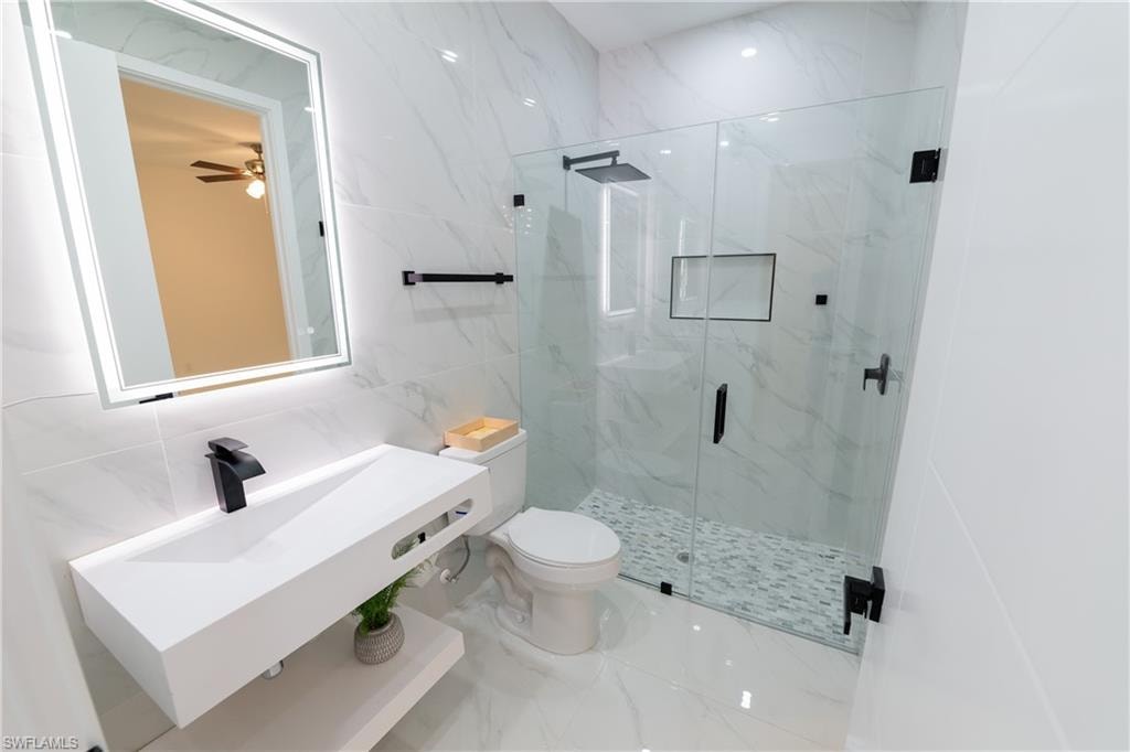 Bathroom with a shower with shower door, sink, tile walls, and toilet