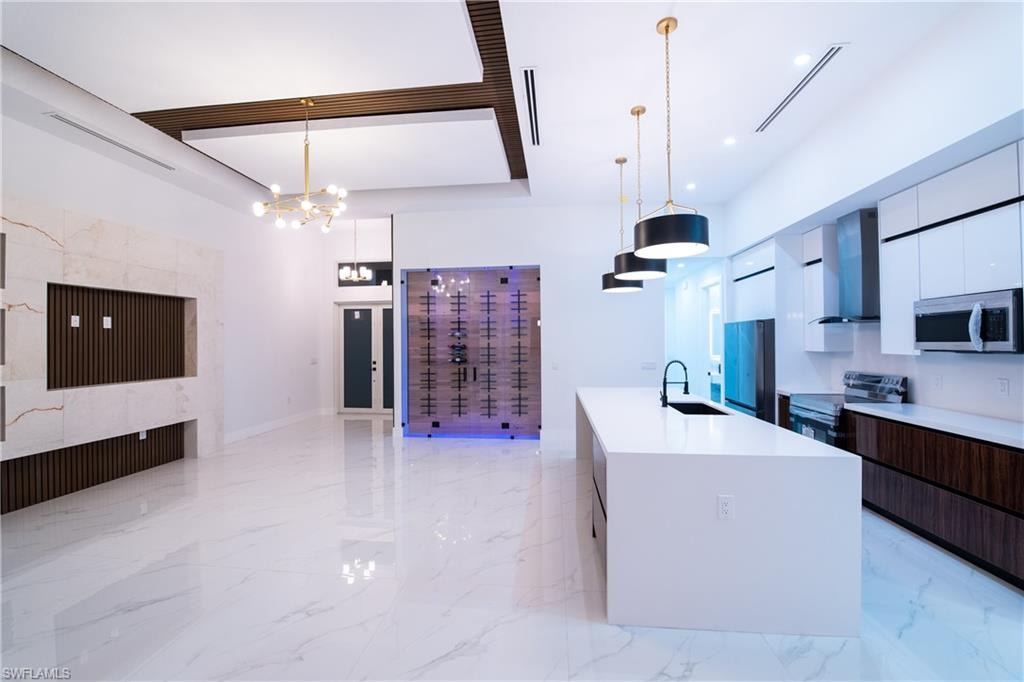 Kitchen featuring appliances with stainless steel finishes, a kitchen island with sink, pendant lighting, and wall chimney exhaust hood