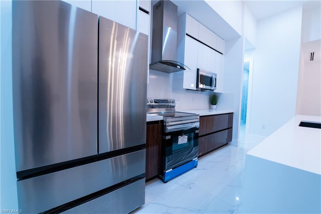 Kitchen featuring white cabinets, stainless steel appliances, and wall chimney exhaust hood