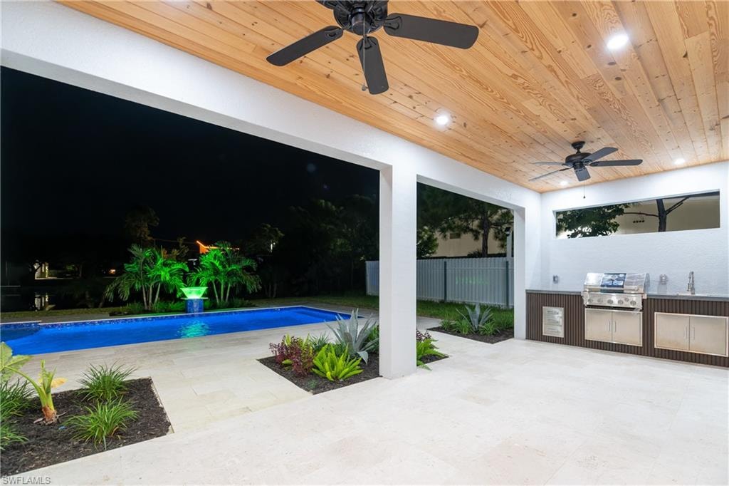 View of swimming pool featuring grilling area, a patio, ceiling fan, and an outdoor kitchen