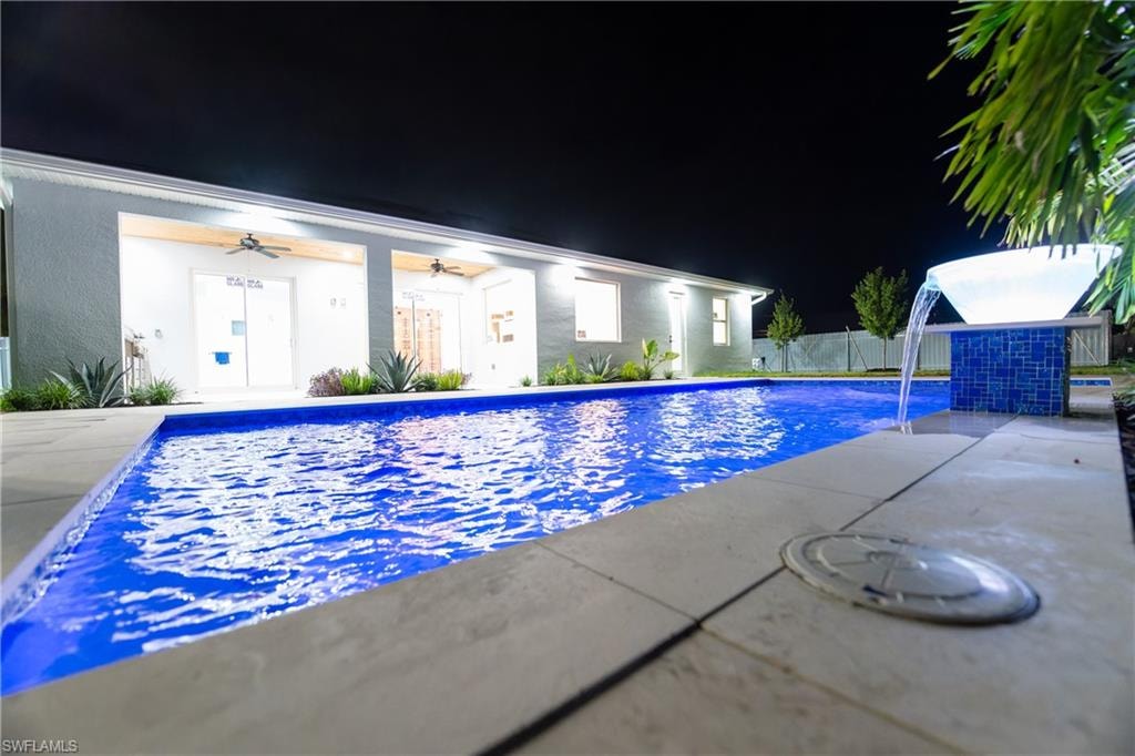Pool at twilight featuring pool water feature, ceiling fan, and a patio