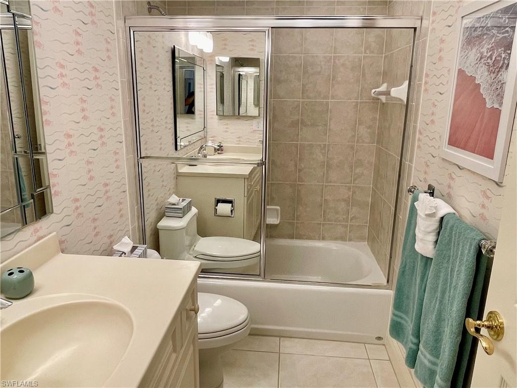 Full bathroom with tile patterned flooring, vanity, toilet, and combined bath / shower with glass door