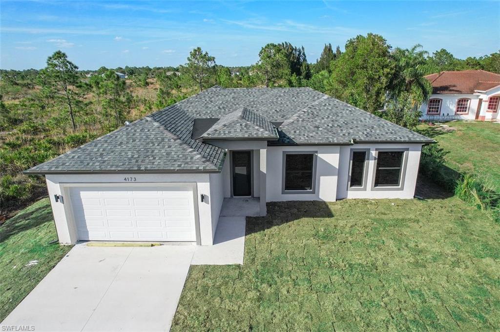 Ranch-style house with an attached garage, driveway, roof with shingles, stucco siding, and a front lawn