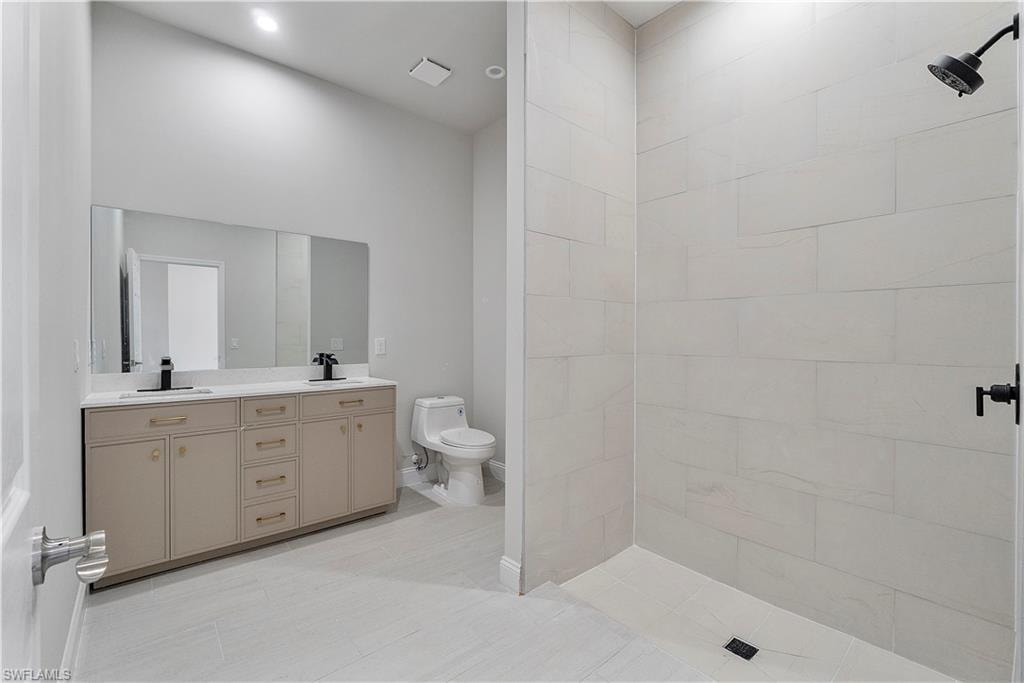 Bathroom featuring tiled shower, a sink, toilet, and double vanity