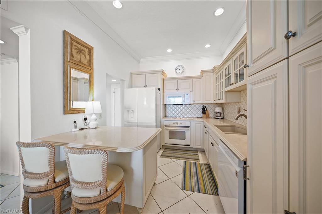 Kitchen featuring a breakfast bar, sink, backsplash, crown molding, and white appliances