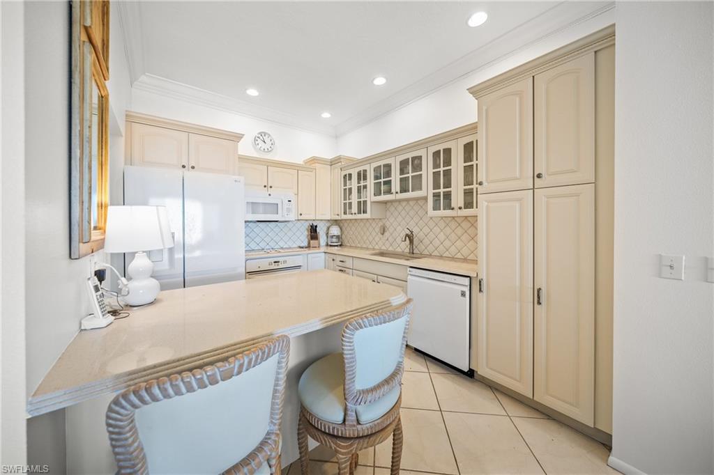 Equipped Kitchen featuring white appliances, a breakfast bar area, light tile patterned floors, and pillow tile  backsplash