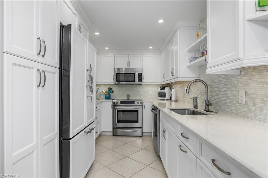 Kitchen with sink, white cabinets, light tile patterned floors, light stone counters, and stainless steel appliances