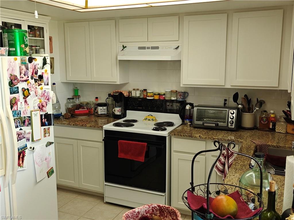 Kitchen featuring light tile patterned floors, dark stone countertops, range with electric cooktop, white refrigerator with ice dispenser, and decorative backsplash