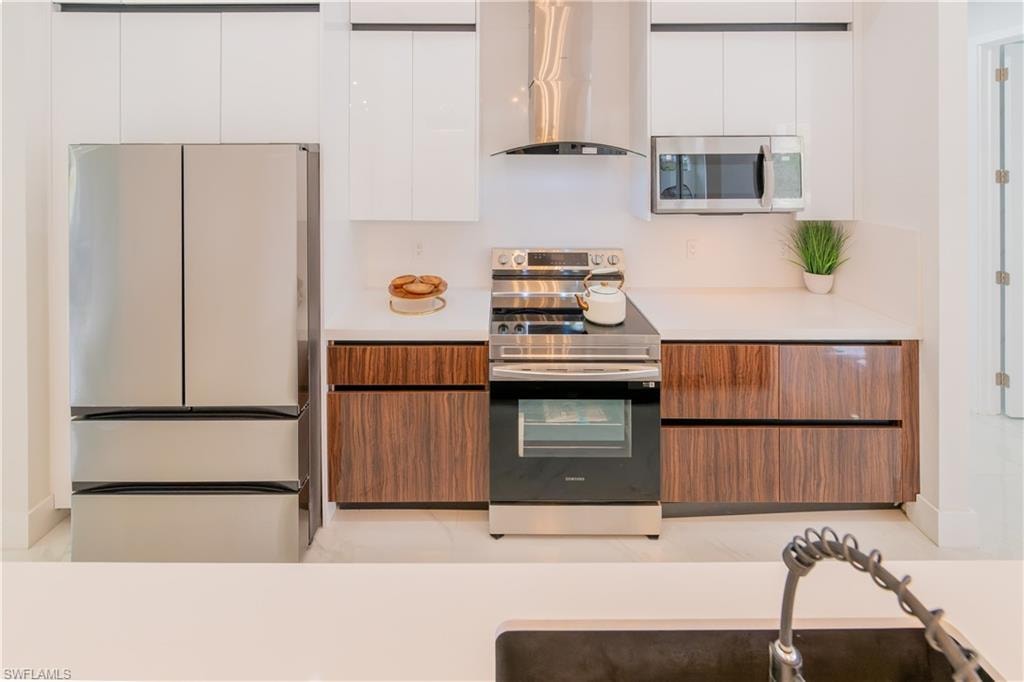Dual tone kitchen featuring stainless steel appliances, two tone cabinetry, range hood, and modern cabinets