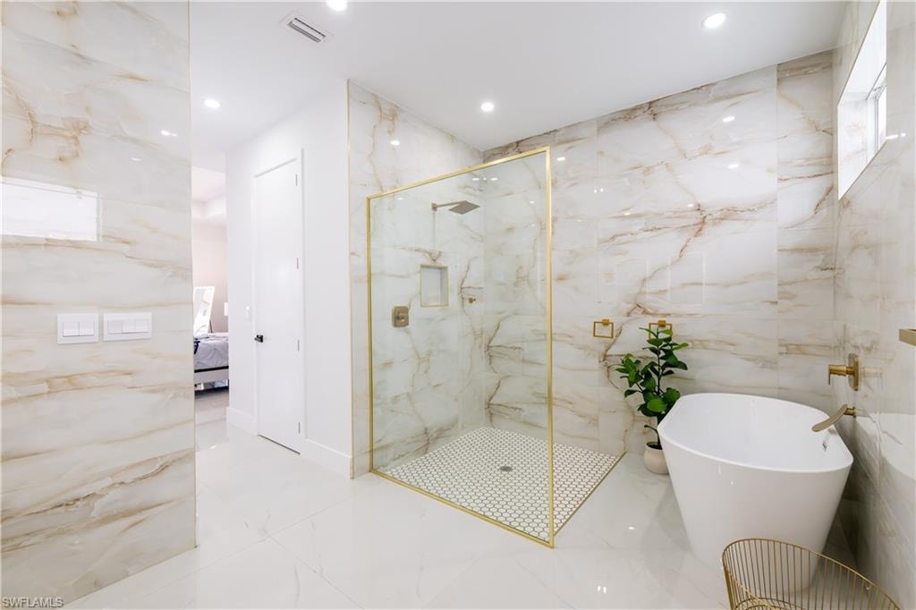 Bathroom featuring stone wall, a marble finish shower, light marble finish floors, recessed lighting, and tile walls