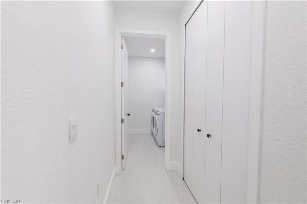 Corridor with a textured wall, washing machine and dryer, light marble finish flooring, and recessed lighting