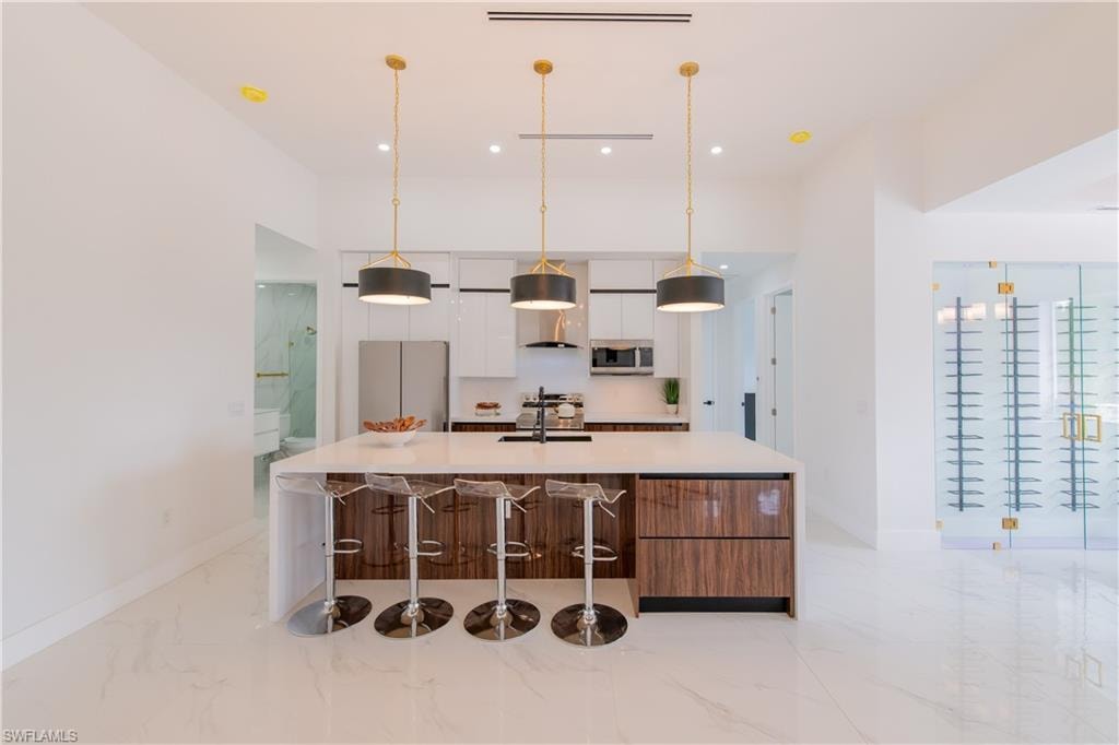 Kitchen featuring a large island, modern cabinets, light marble finish floors, a kitchen bar, and freestanding refrigerator
