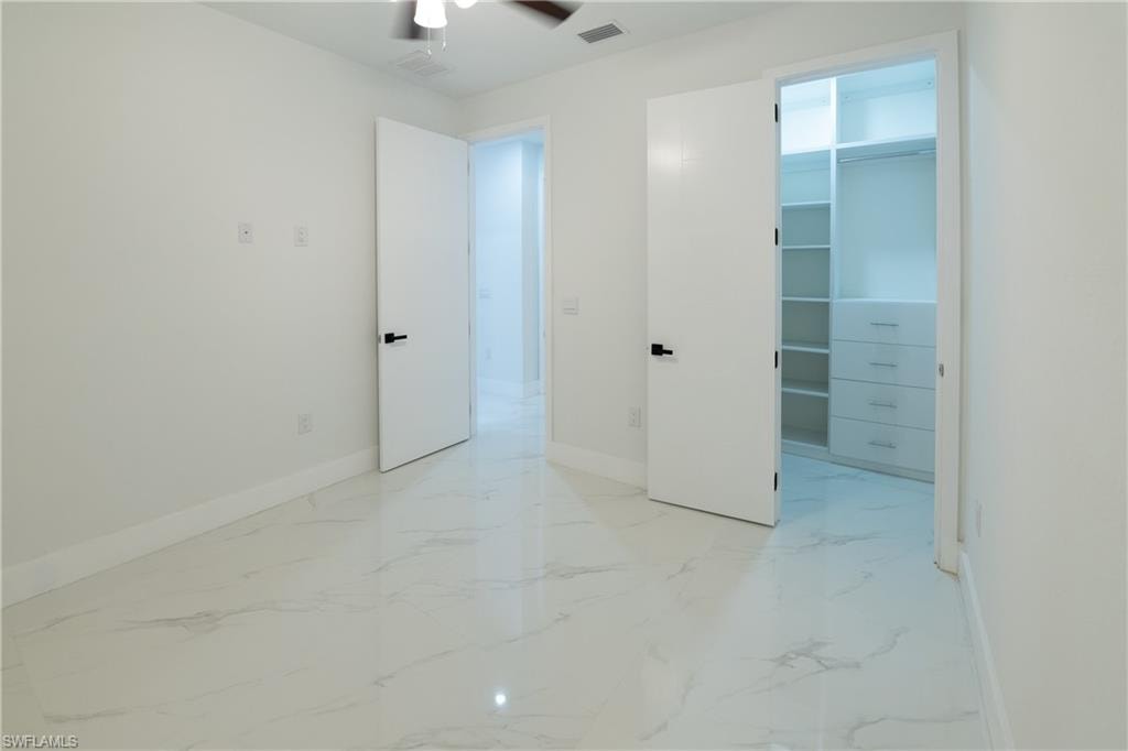 Unfurnished bedroom featuring a walk in closet, a closet, and ceiling fan