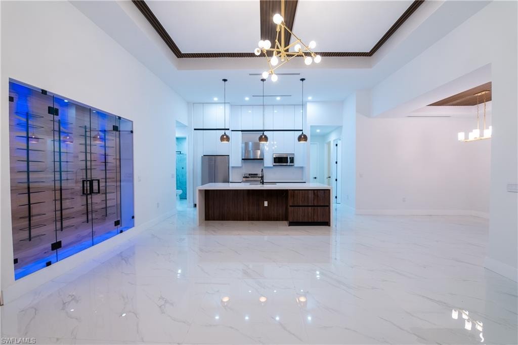 Kitchen with a large island with sink, a tray ceiling, a notable chandelier, and stainless steel appliances