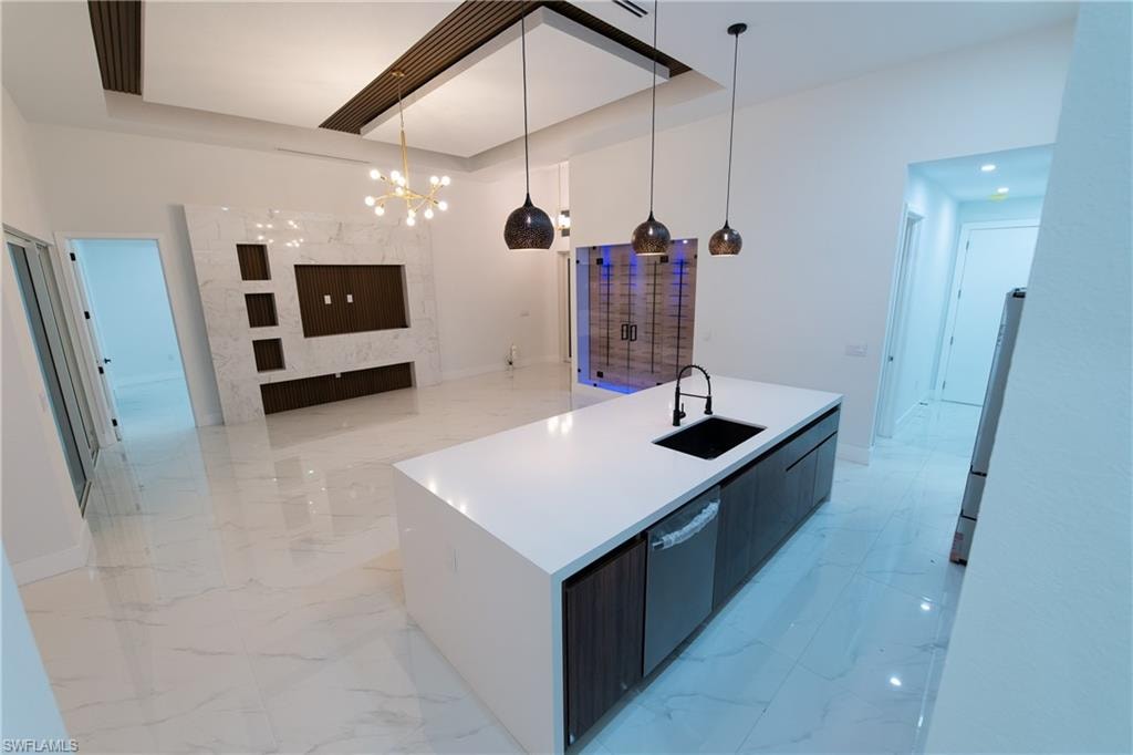 Kitchen with sink, hanging light fixtures, stainless steel dishwasher, an island with sink, and white fridge