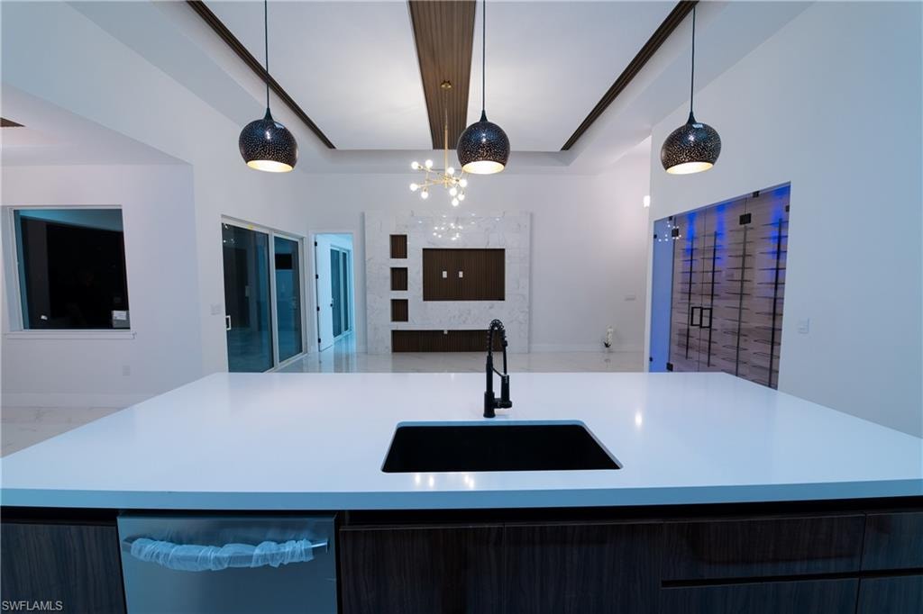 Kitchen featuring pendant lighting, dishwasher, sink, a kitchen island with sink, and a tray ceiling