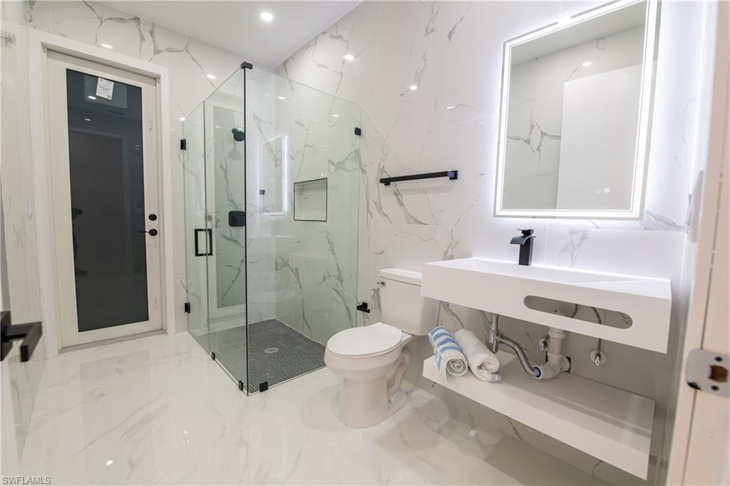 Bathroom featuring an enclosed shower, sink, and toilet